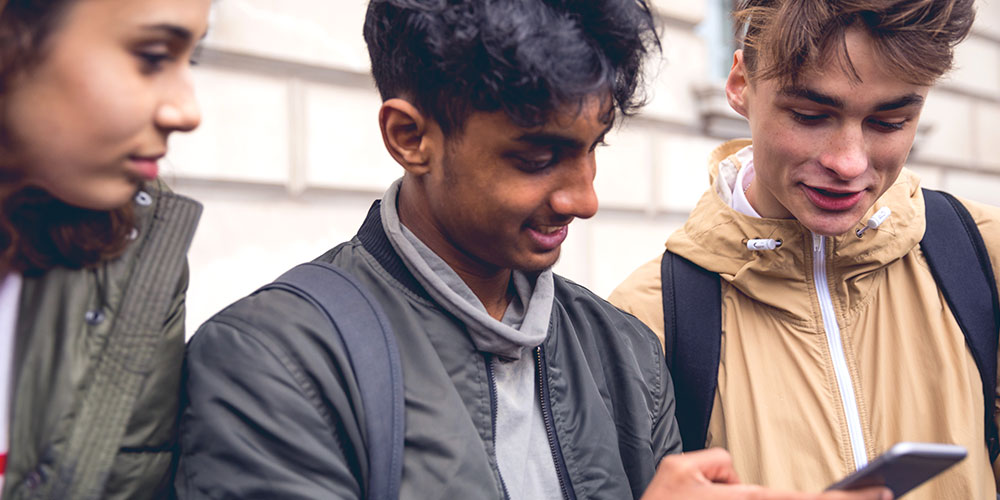 three teens smiling while looking at a cell phone